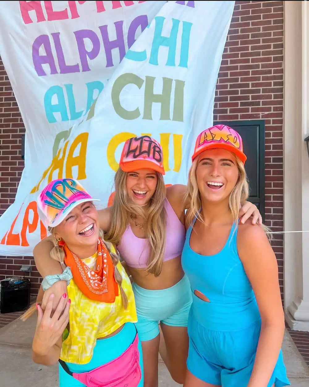 Three young women wearing brightly colored athletic wear and hats.